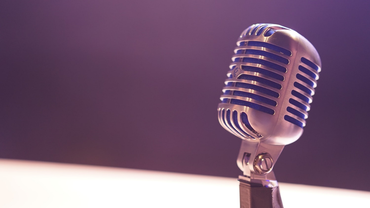 A metallic microphone glistens under soft purple light