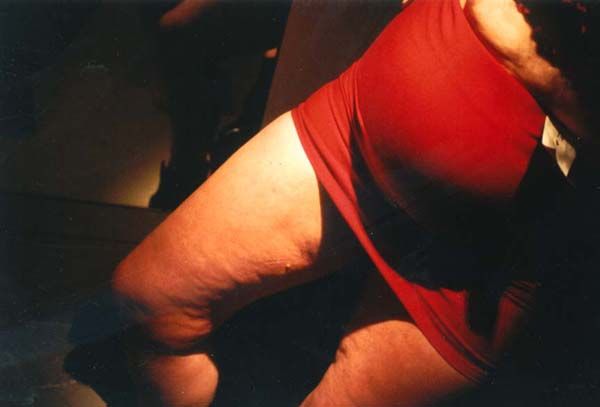 A white woman's legs and belly is shown. She is wearing a tight red skirt and something looking like a note or a playing card is sticking out.