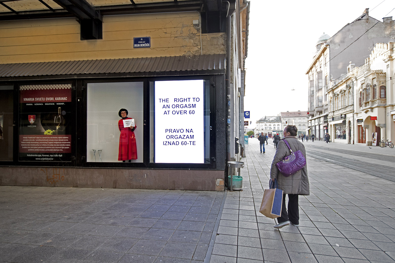 The artist is standing in a shop window in a long, red dress, next to a sign that reads The right to orgasm at over 60 in big, bold letters.